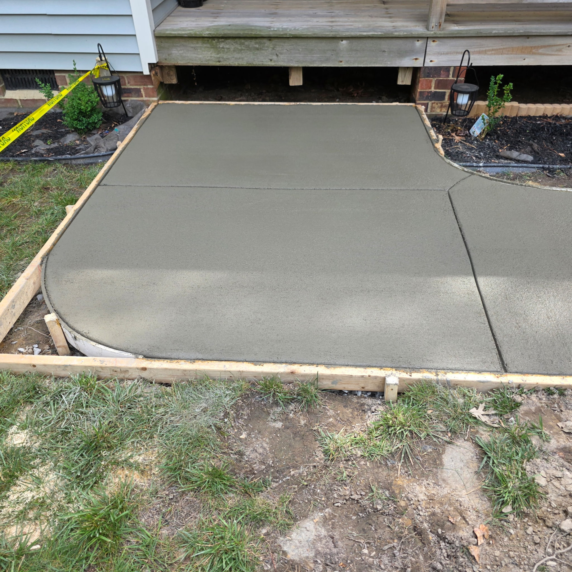 Freshly poured concrete walkway with clean saw-cut joints and a curved edge beneath a home's entry landing