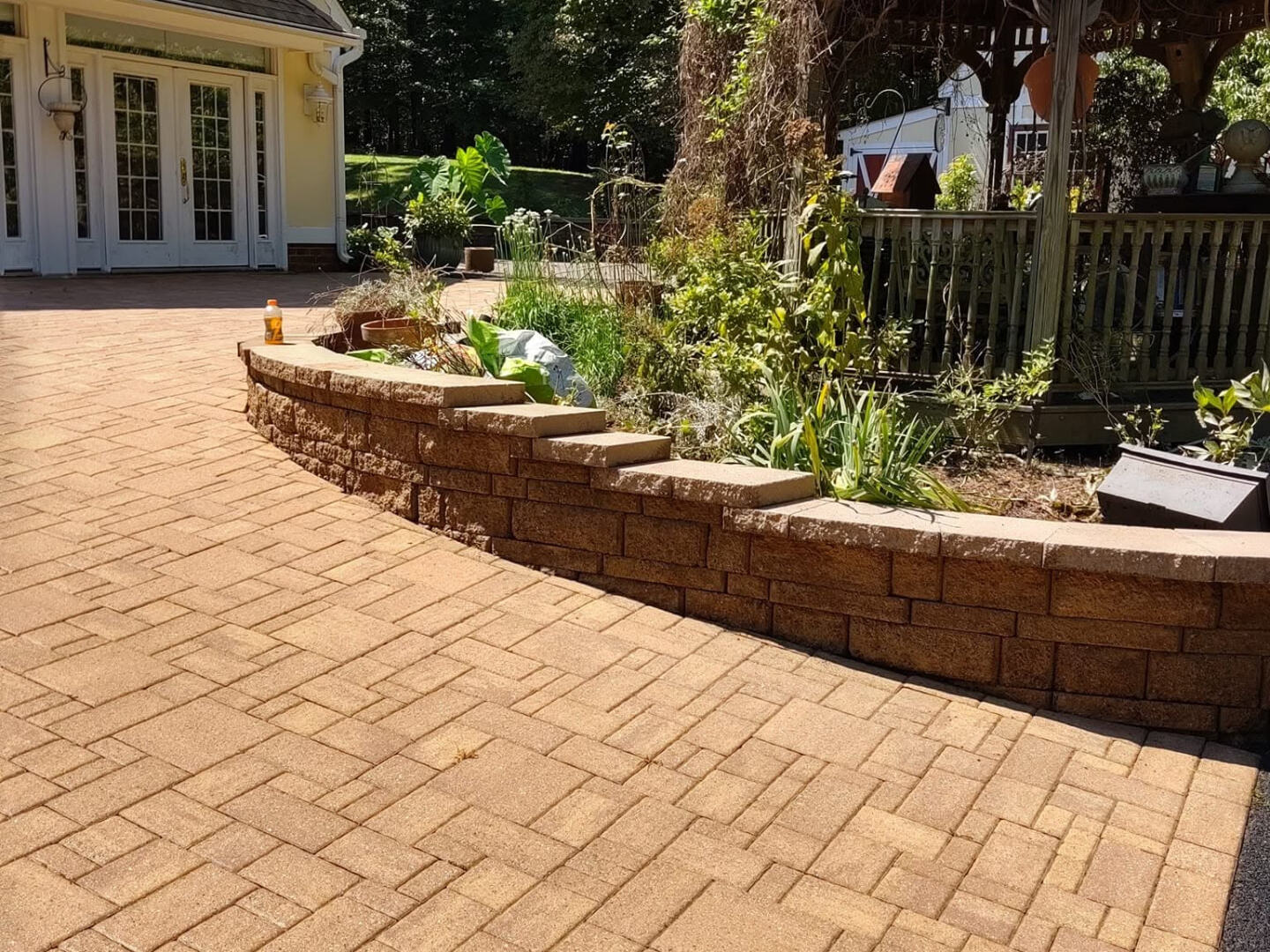 Paver patio with a curved block retaining wall, planting beds, and a gazebo beside a Virginia home