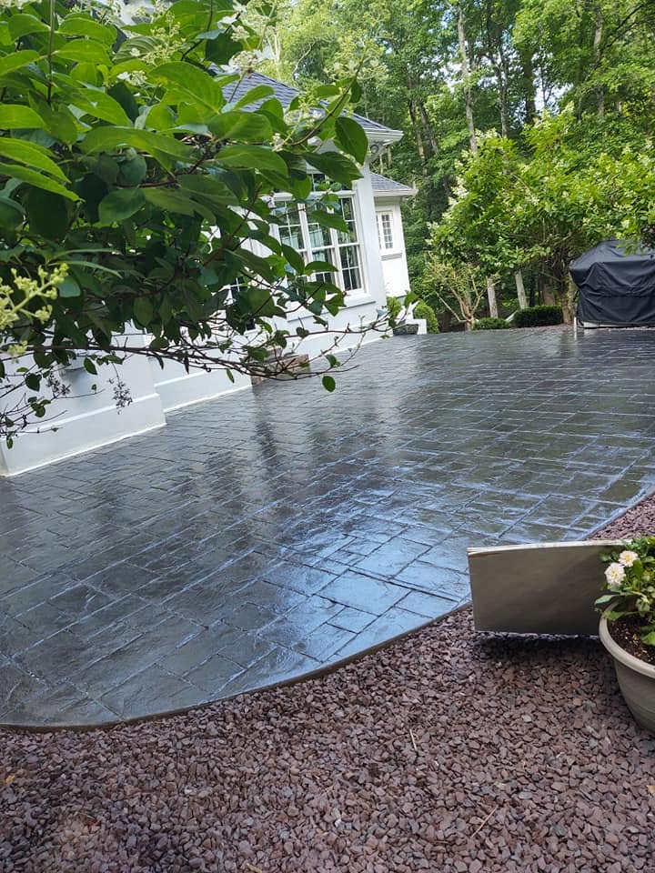 Stamped concrete surface with a stone pattern curving beside a white home and garden beds
