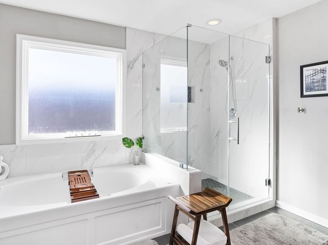Bright renovated bathroom with a soaking tub, glass shower, and marble finishes