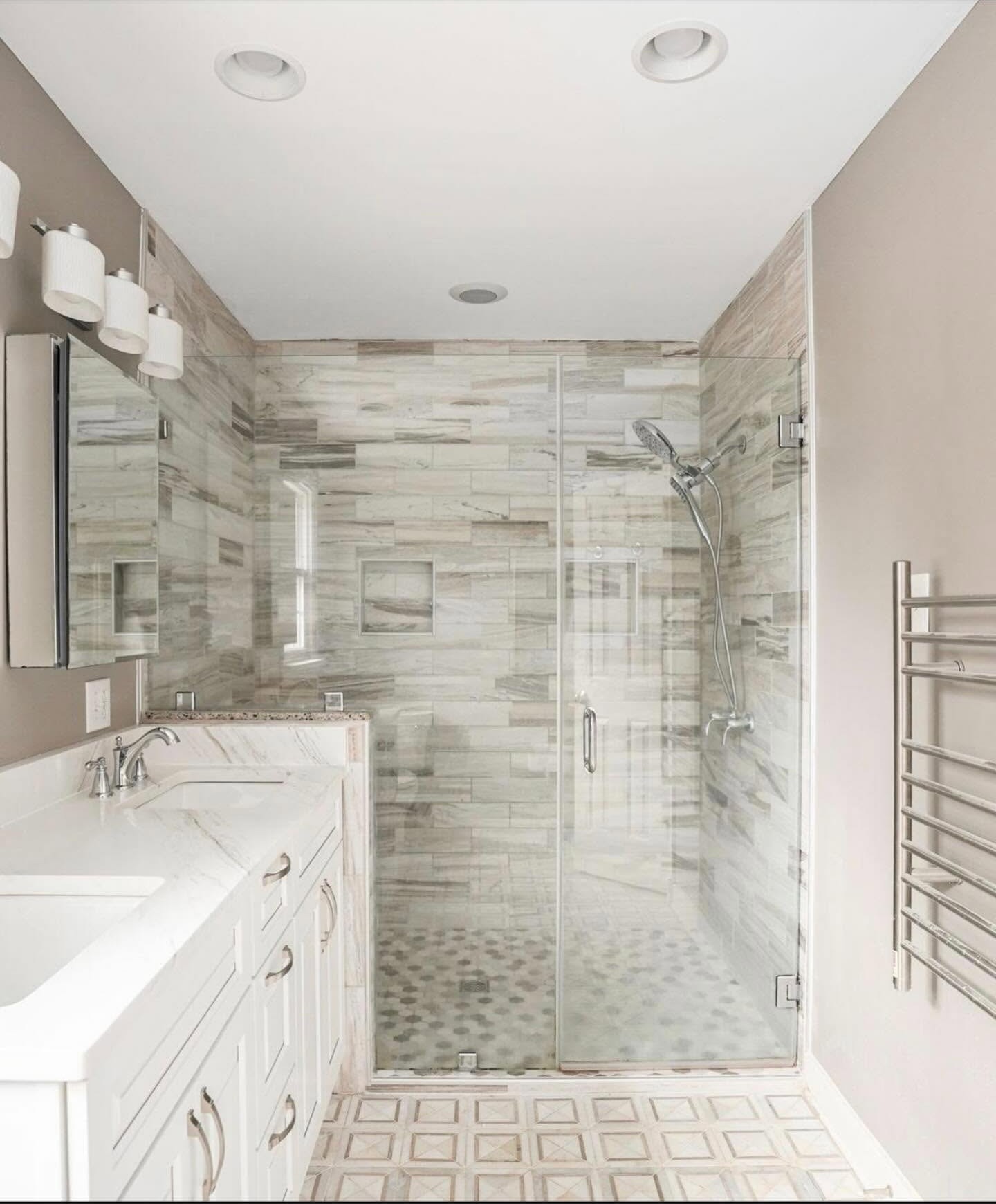 Walk-in shower finished in warm marble-look tile with a glass enclosure and patterned floor