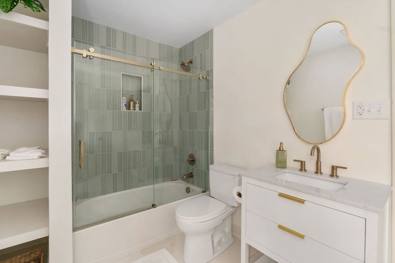 Renovated bathroom with sage green vertical tile, a glass shower, and warm brass fixtures