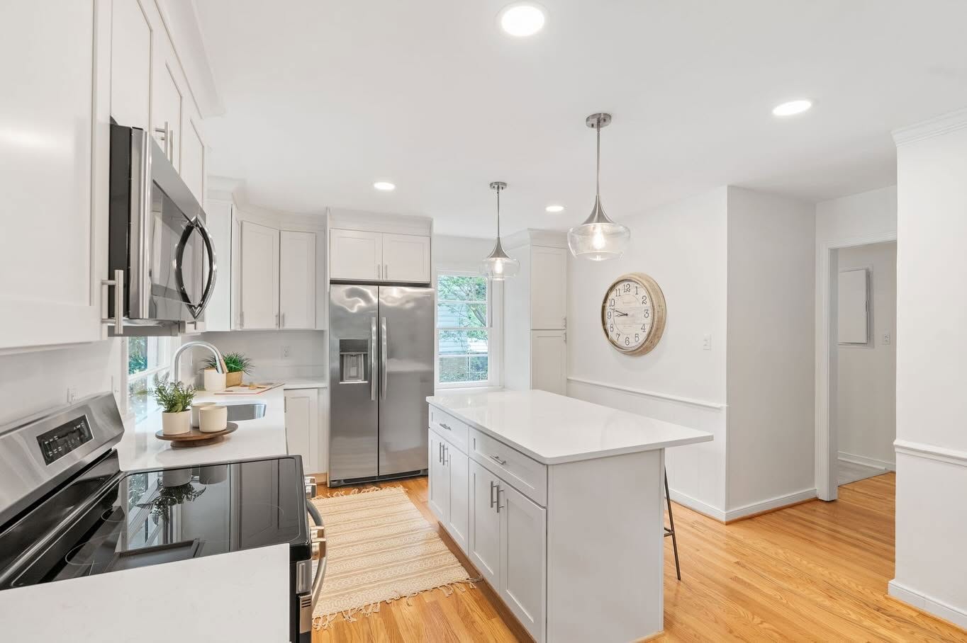 Bright renovated kitchen with white cabinetry, quartz countertops, a central island, stainless steel appliances, and hardwood floors