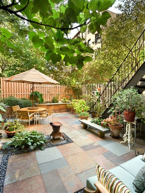 Small courtyard patio with bluestone pavers, potted plants, outdoor seating, and a striped umbrella tucked beneath leafy trees