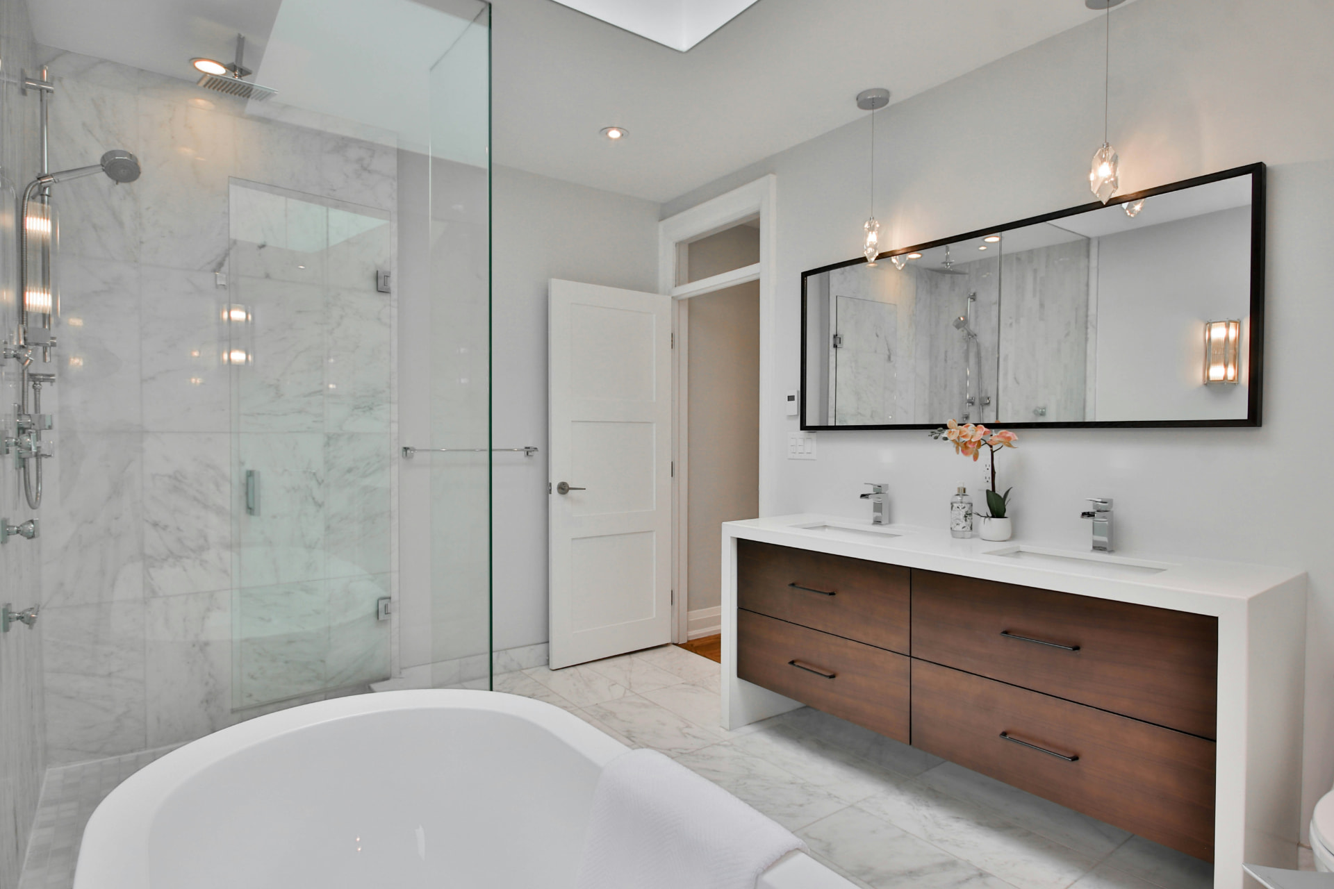 Primary bathroom with a freestanding white tub, a glass walk-in shower, and a dark wood double vanity beneath pendant lights