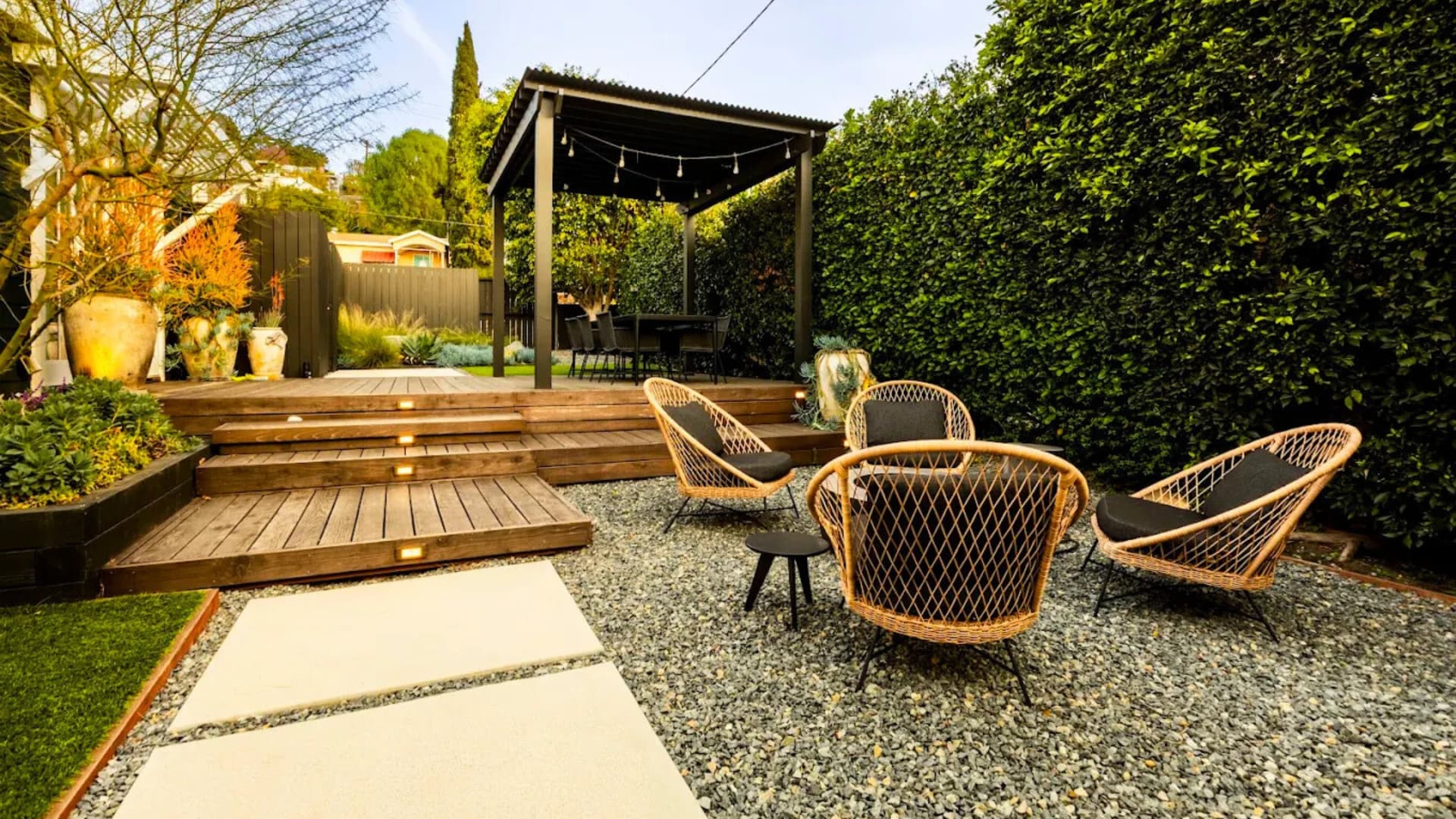 Modern deck with integrated wood steps, gravel courtyard, woven lounge seating, and a pergola in a private backyard