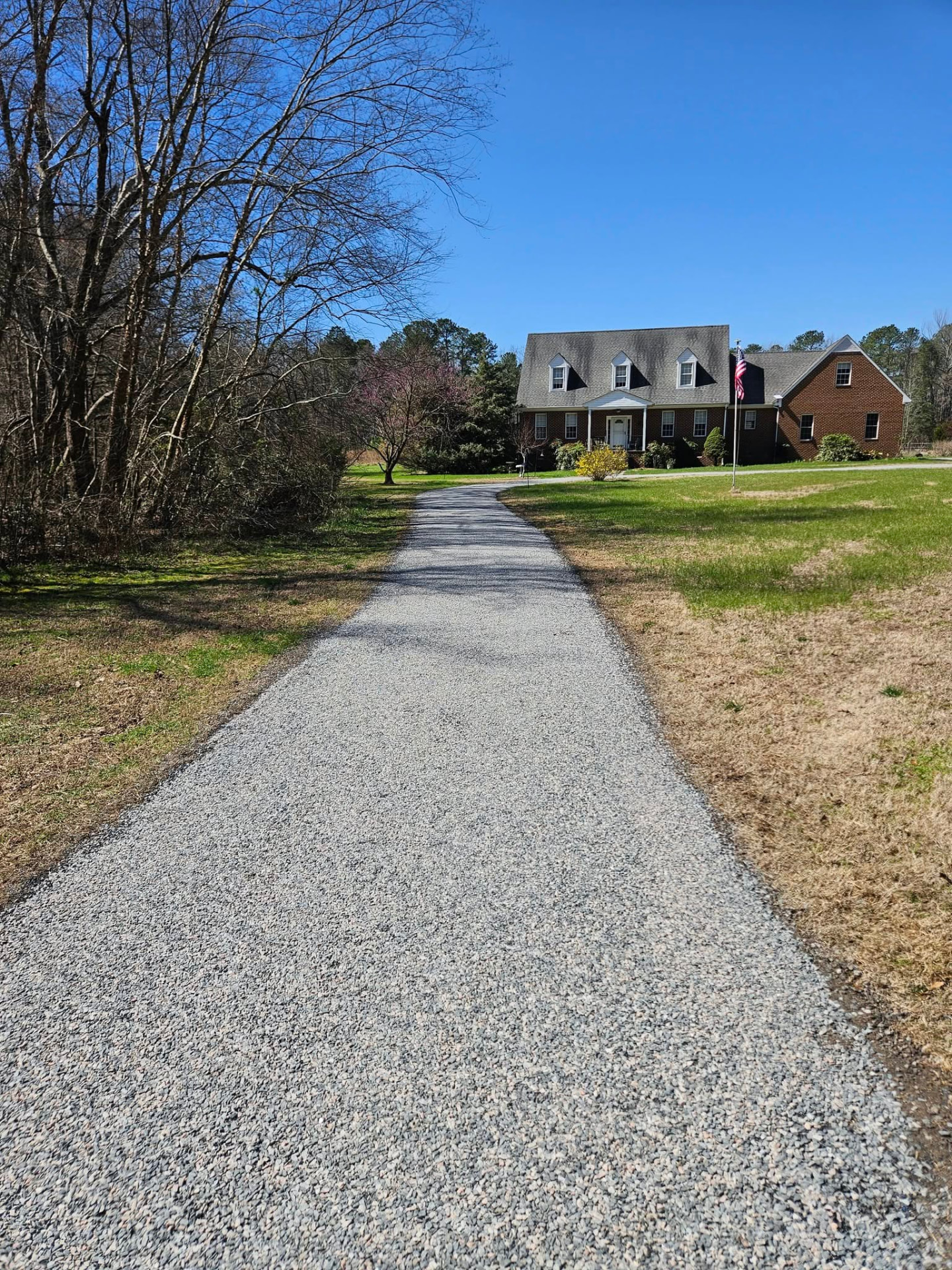 Long gravel driveway leading to a brick Virginia home beneath a clear blue sky