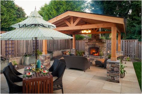 Outdoor dining table beside a timber pavilion with a stone fireplace and warm evening lighting