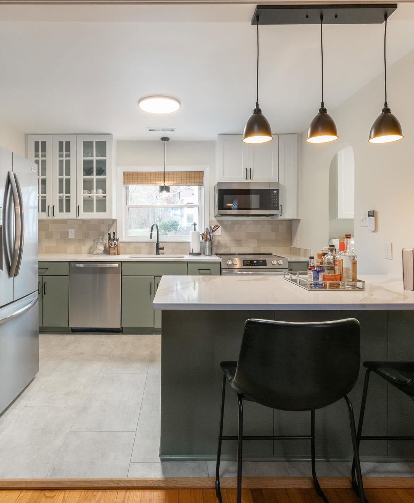 Renovated kitchen with sage-green lower cabinets, white upper cabinets, a dark island, pendant lights, and counter seating