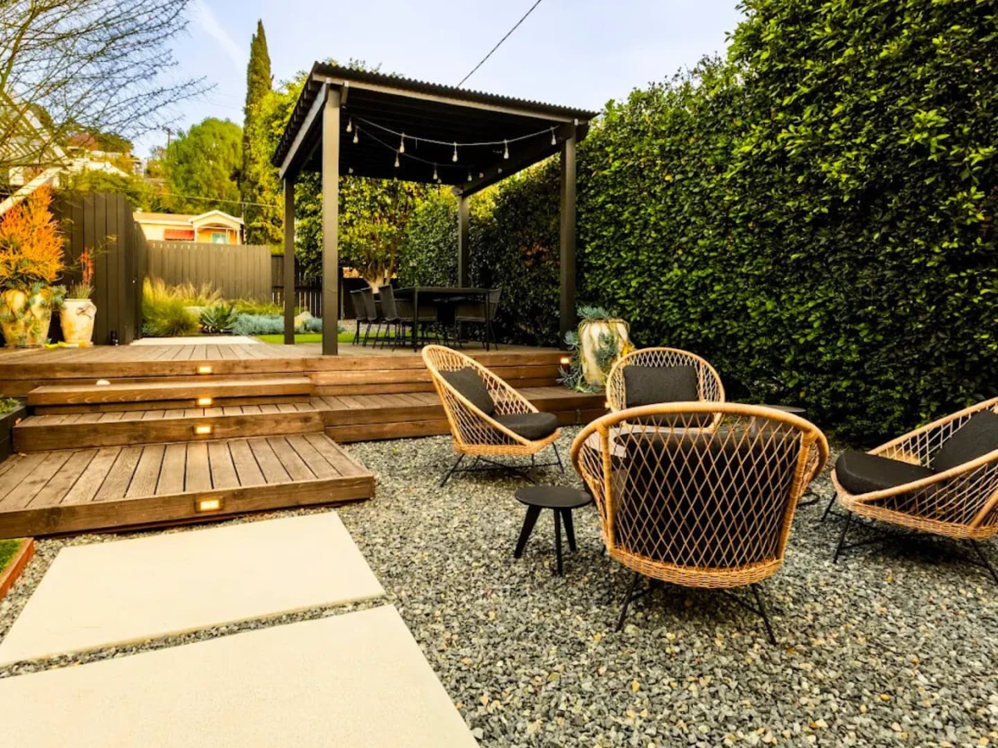 Modern deck with a dark pergola, string lights, and woven lounge seating around a gravel courtyard